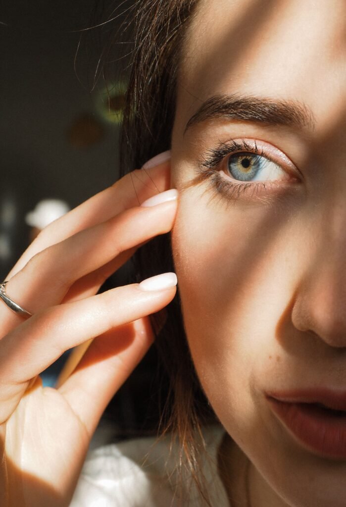 Close-up photo of a woman's blue eye and hand with sunlight creating patterns on her face.